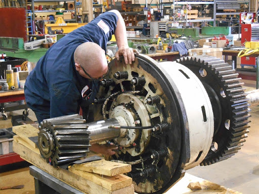 Skilled mechanical engineer repairing industrial machine part with precision tools in a workshop setting"